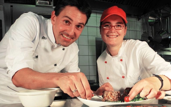 Alexander Bösch und die Köchin vom Gasthaus Adler lächeln, während sie eines der Gerichte von der Speisekarte anrichten